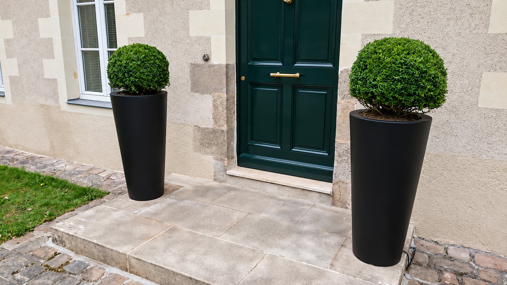 Deux grands pots noirs avec buis taillés en boule devant une porte d’entrée verte à Nantes